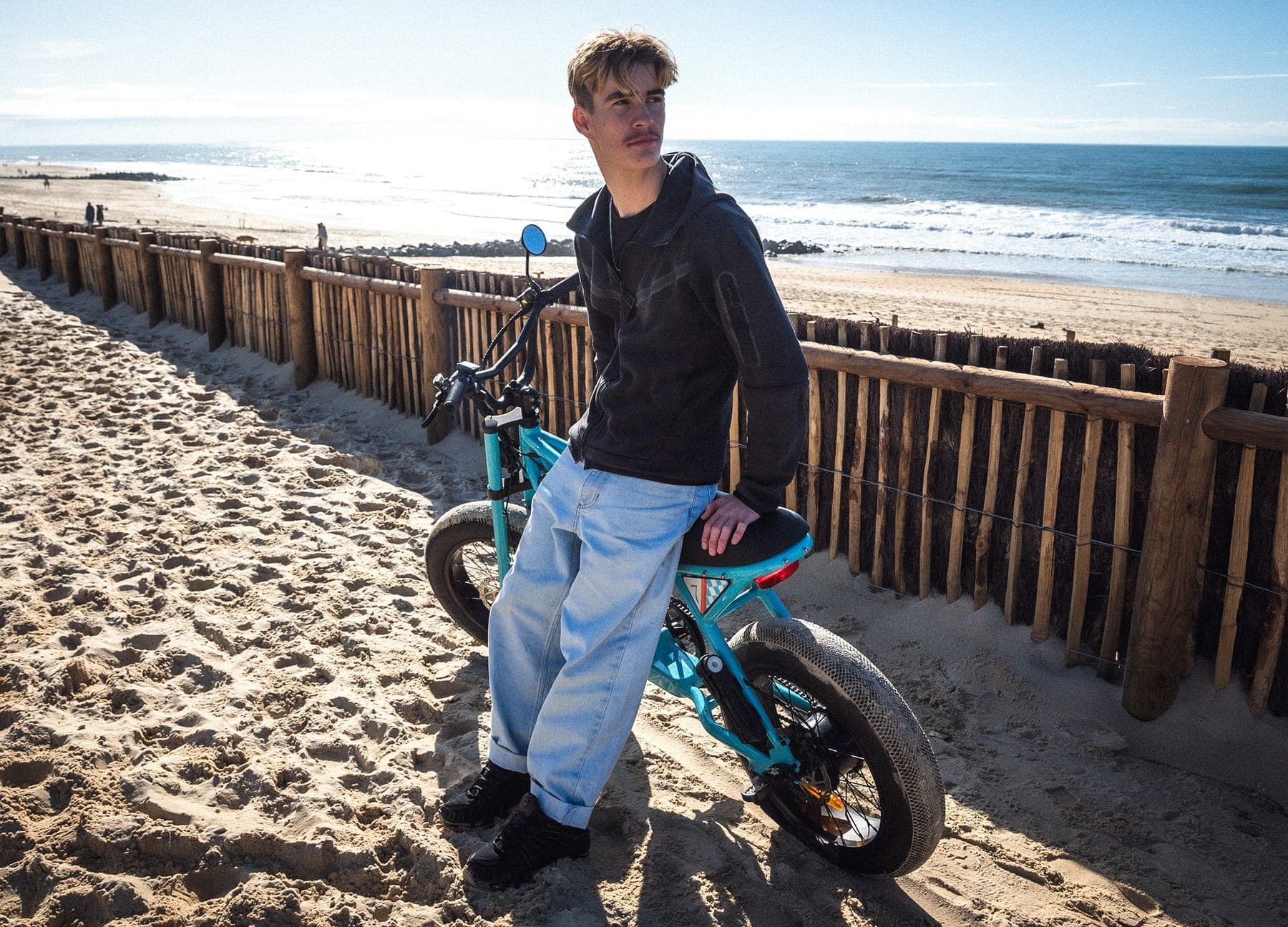 The Ponyboy leaning against a fence by the dunes