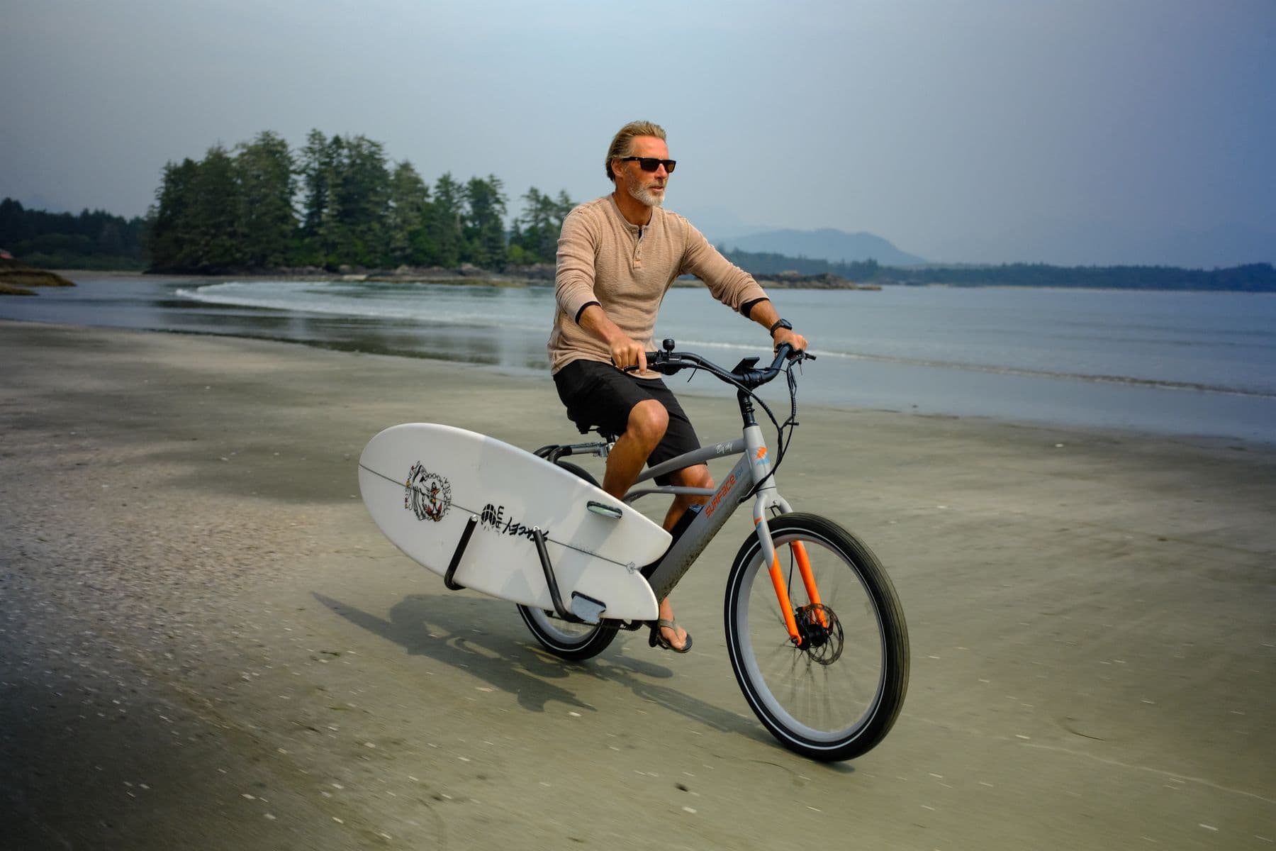 Rider carrying a surfboard on a Surface 604 cruiser along the beach