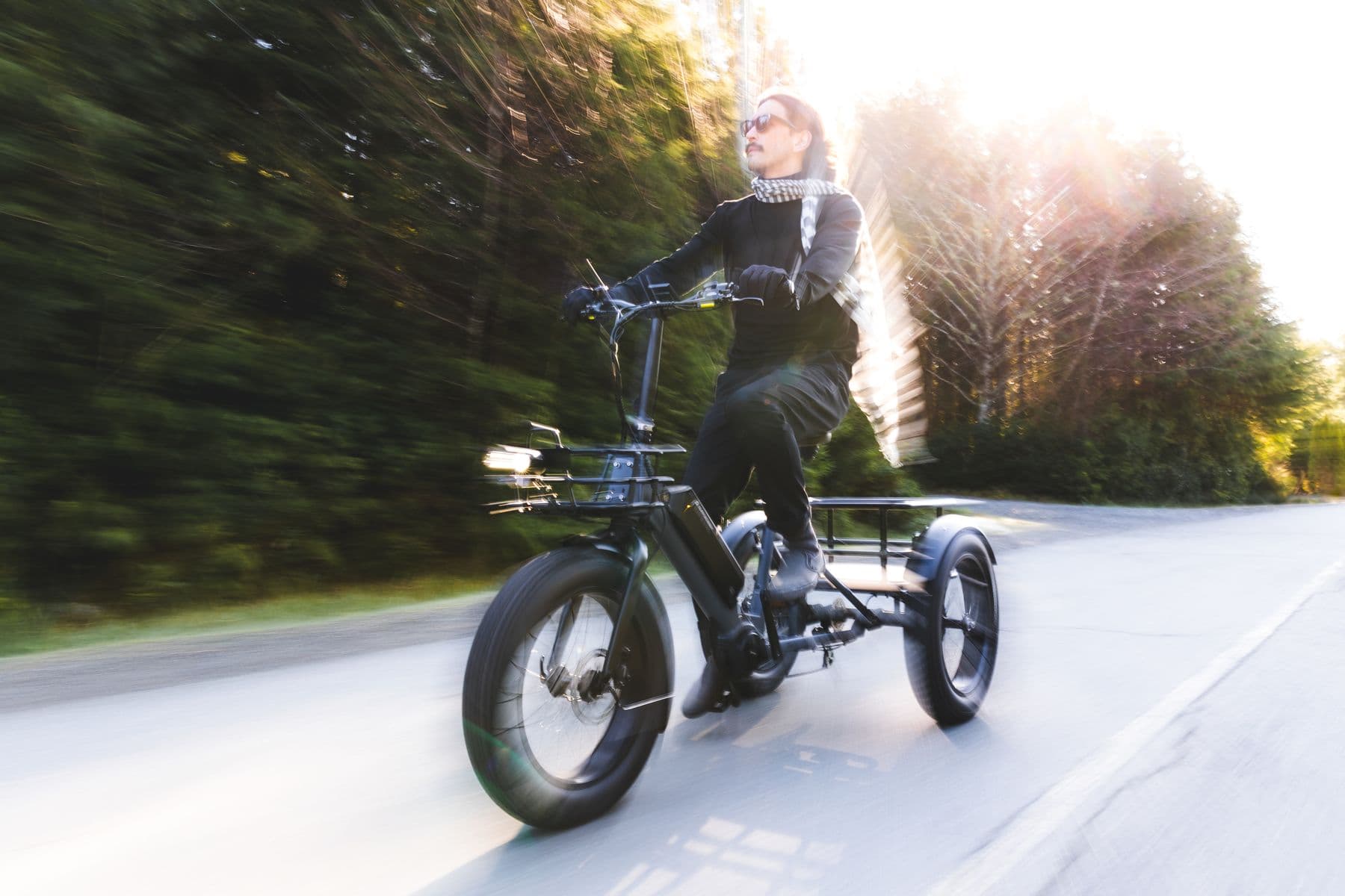 Rider on a Surface 604 cargo trike moving fast down a tree-lined road